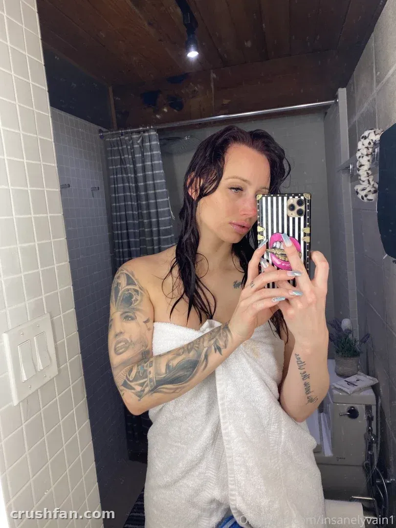 Moneybirdette VIP in a white towel taking a mirror selfie in a tiled bathroom