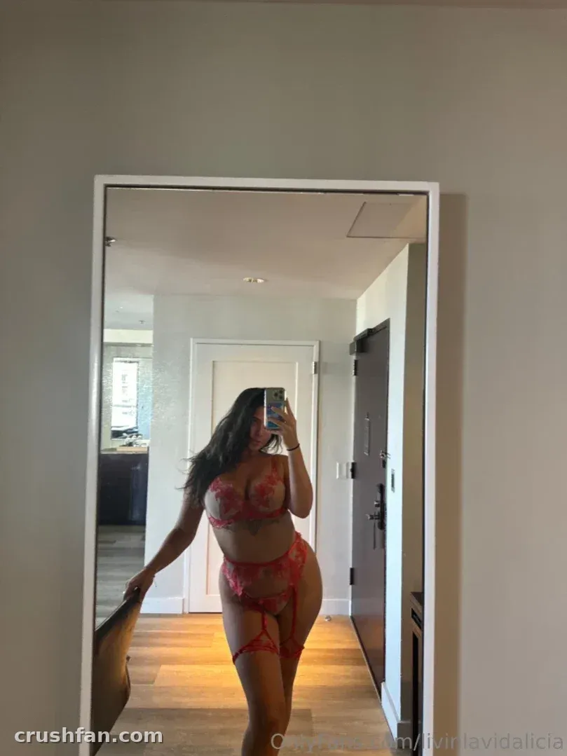 Alicia se toma una selfie en el espejo con lencería de encaje rojo en un pasillo luminoso.