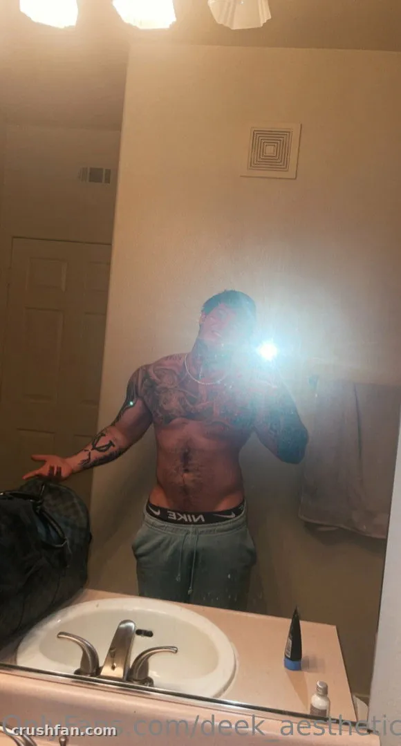 DEEK AESTHETIC taking a shirtless mirror selfie in a bathroom with a bright flash.