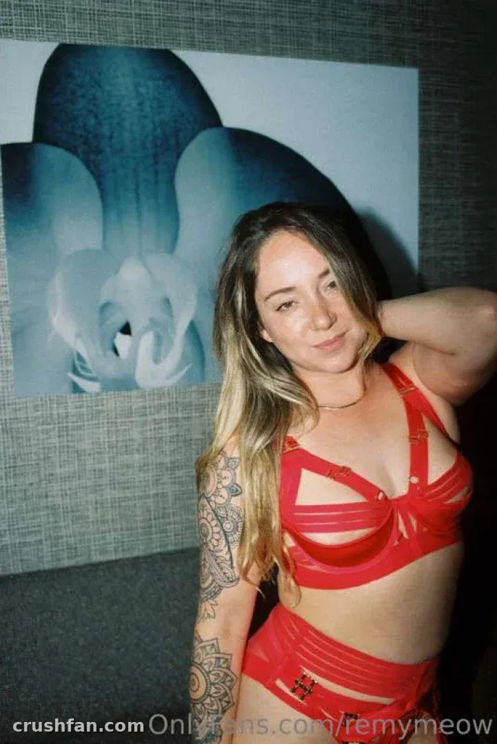 Remy LaCroix in roter Riemchen-Unterwäsche posiert vor einem blauen Orchideen-Druck an einer grauen Wand