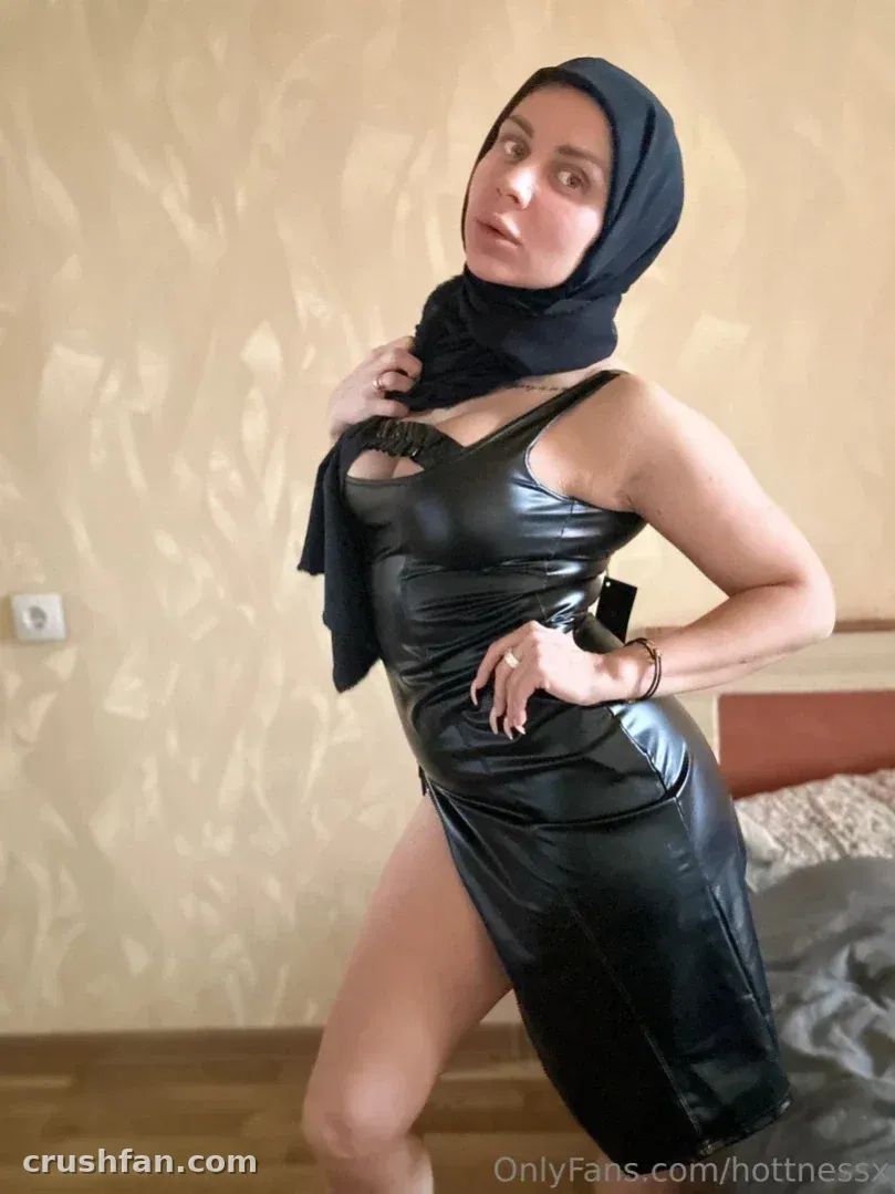 Criadora com hijab preto e vestido preto brilhante posando em ambiente interno
