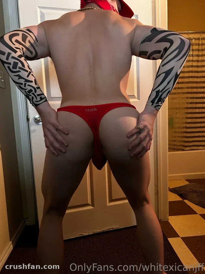 Creator in red thong and cap seen from behind in a doorway, arms tattooed
