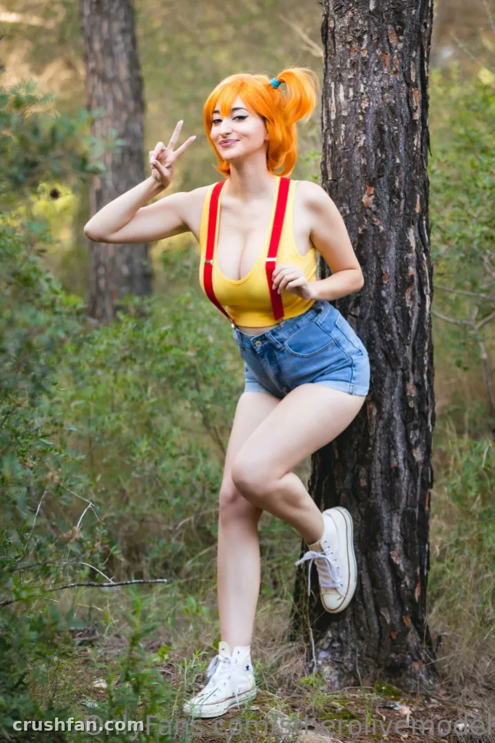 Esther Olivé com um top amarelo e shorts jeans apoiada em uma árvore em uma floresta