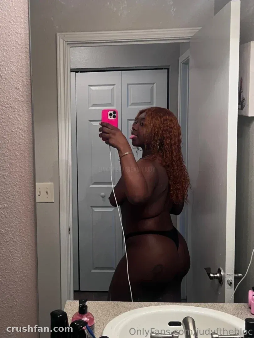 ItzJustJudy tirando uma selfie no espelho em um banheiro usando um conjunto escuro de duas peças.