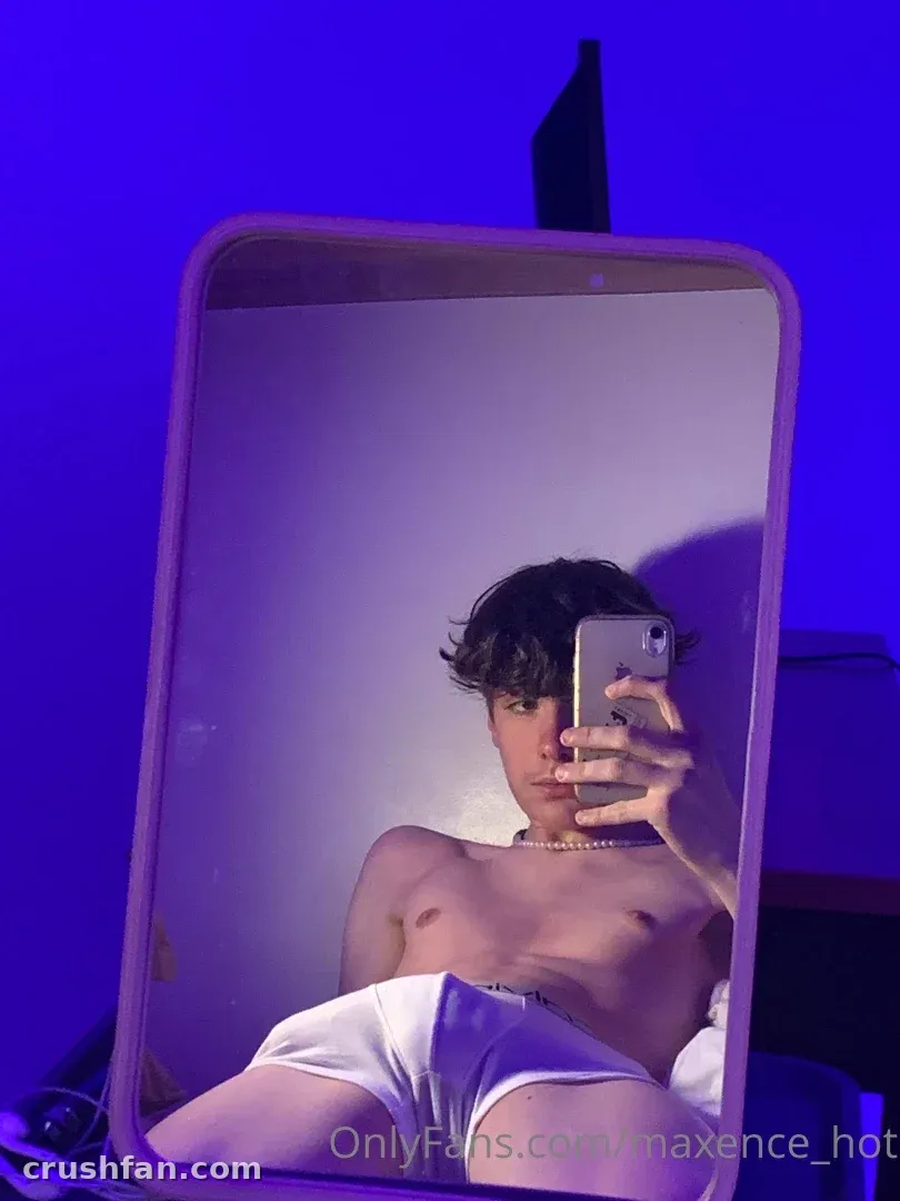 Maxence taking a mirror selfie in purple light wearing a pearl necklace and white shorts.
