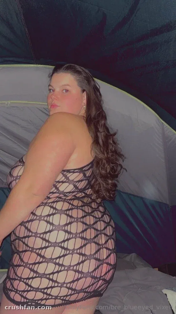 Miss Bunny in a black mesh dress posing inside a tent with grey and blue fabric
