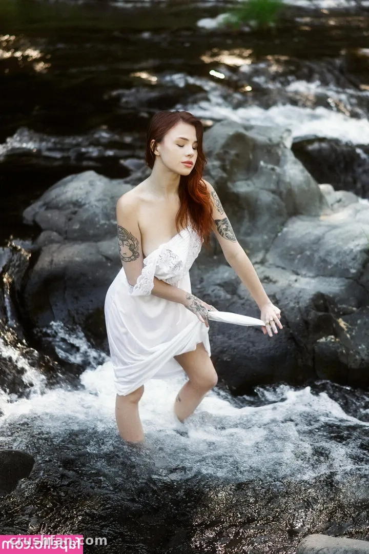 Woman in a white off-shoulder dress standing in a rocky stream with flowing water