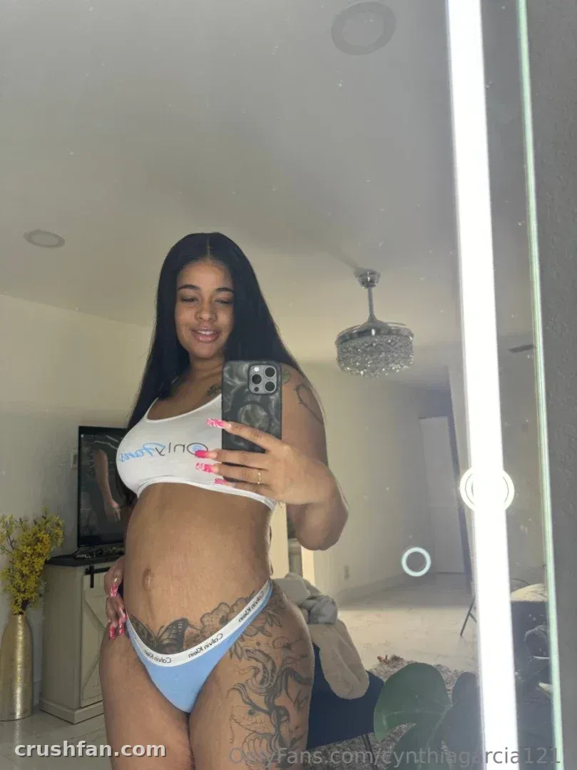 Creator takes a mirror selfie in a white crop top and blue underwear in a bright room.
