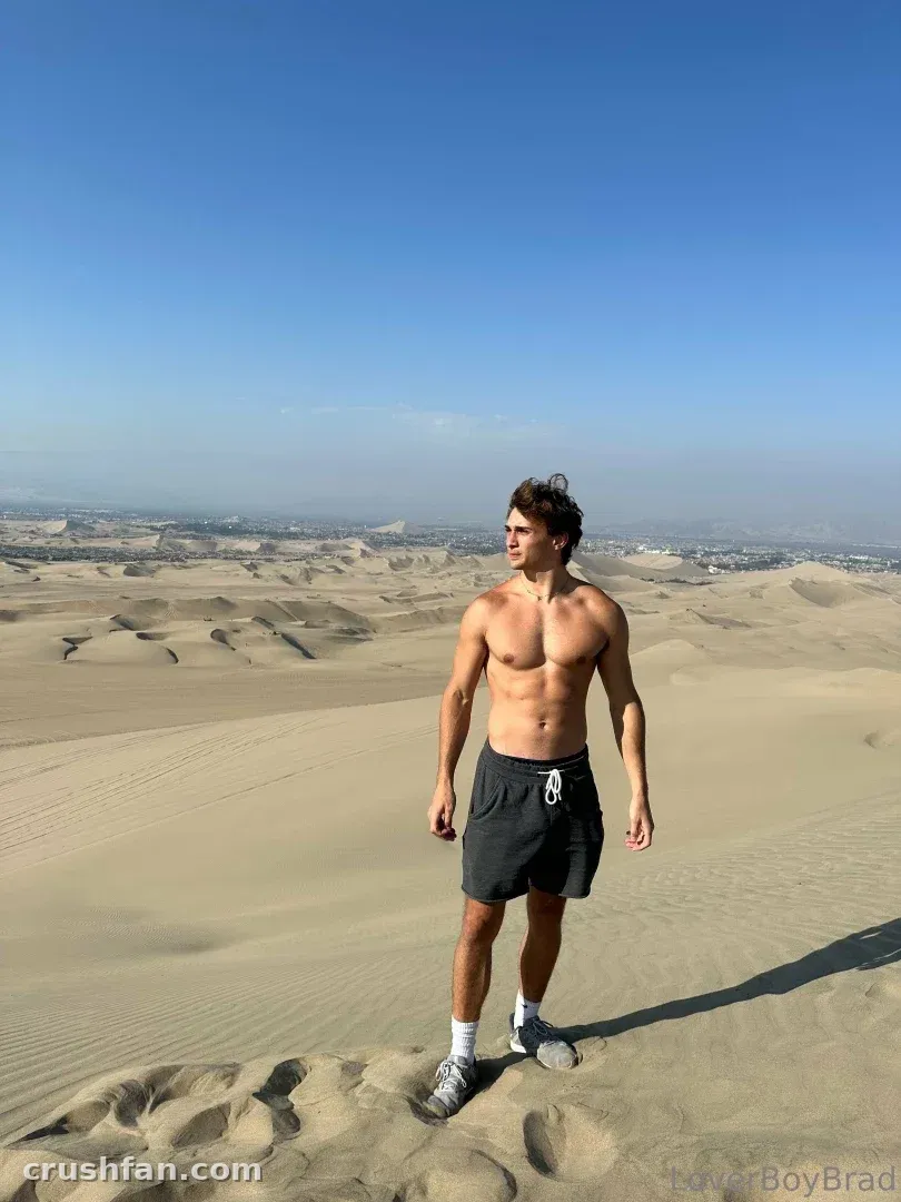 Leo em pé sem camisa em dunas de areia do deserto sob um céu azul claro