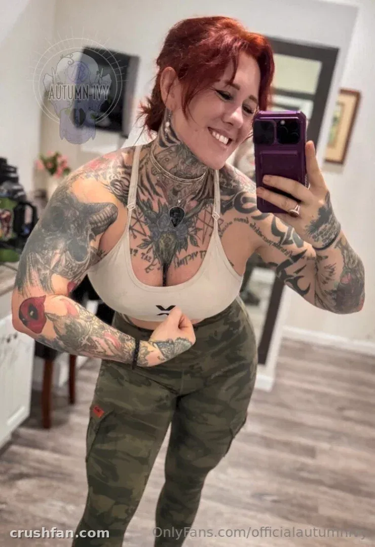 Autumn Ivy sorrindo em uma selfie no espelho usando um top cropped branco e calça de camuflagem
