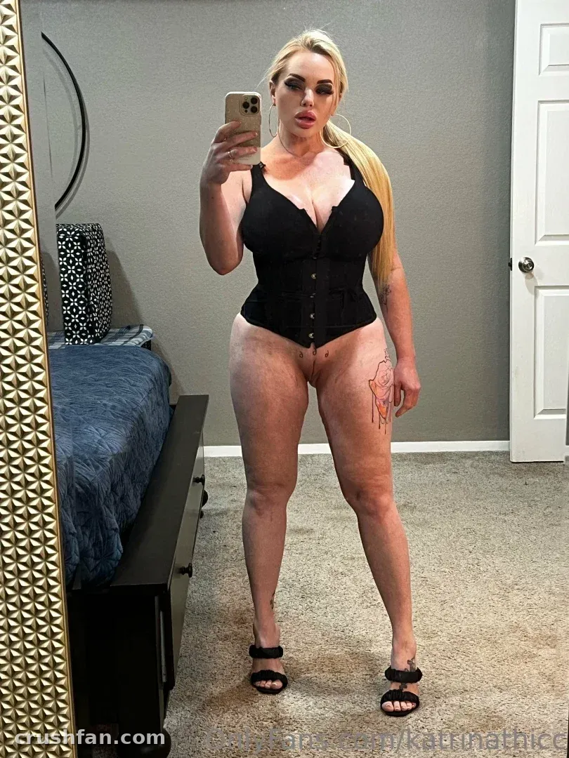 Katrina Thicc in a black corset taking a mirror selfie in a bedroom
