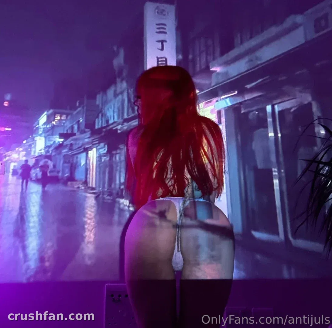 Juls aux longs cheveux roux vue de dos dans une rue mouillée éclairée au néon la nuit
