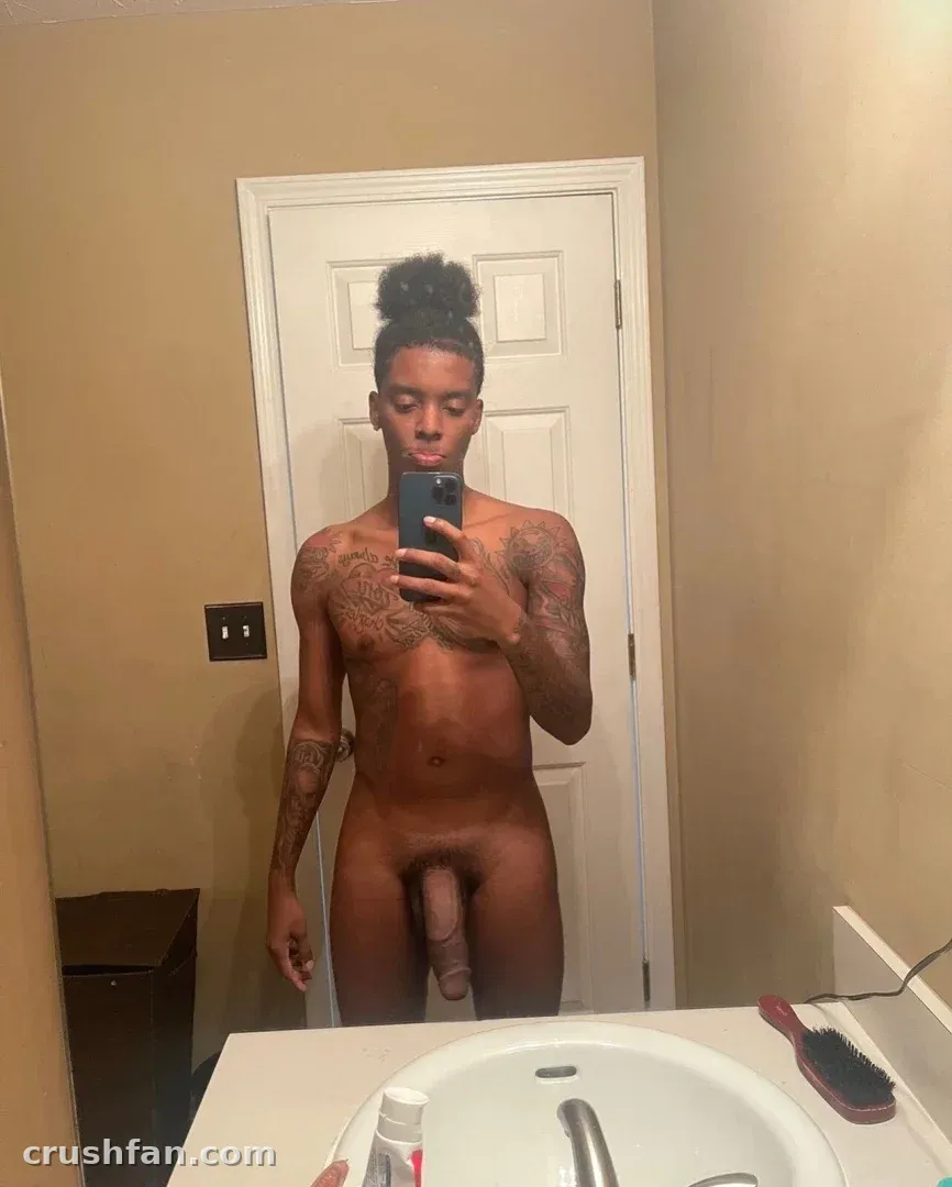 Creator with a hair bun and chest tattoos taking a mirror selfie in a bathroom