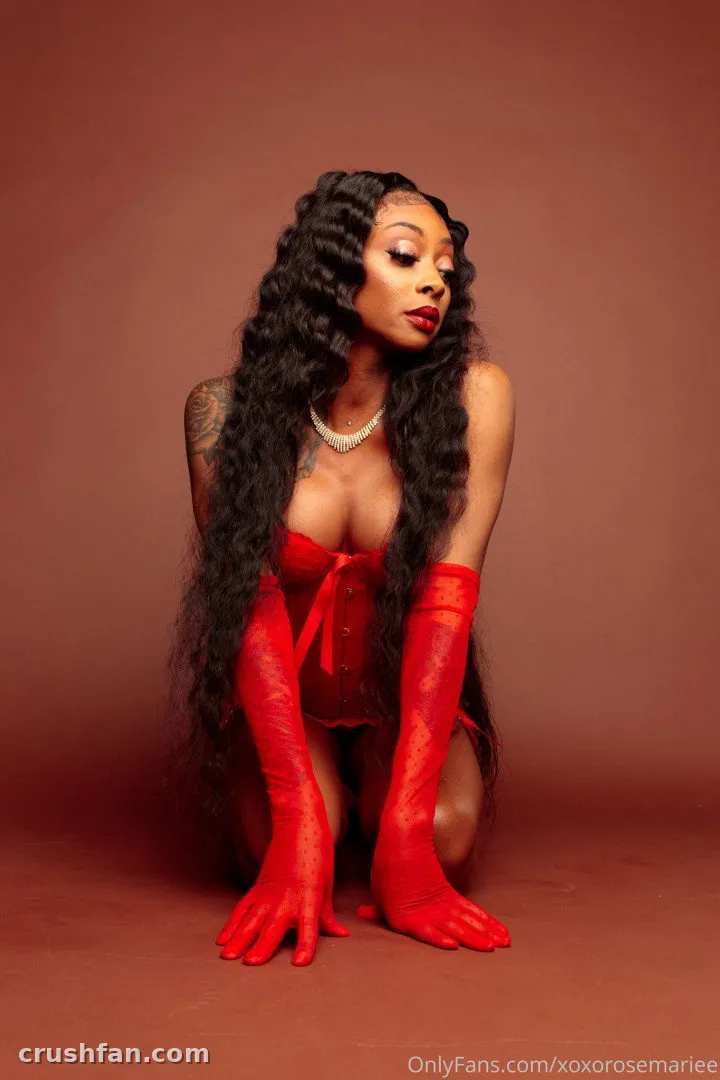 Persuasian kneeling in red lingerie and long red gloves against a warm studio backdrop