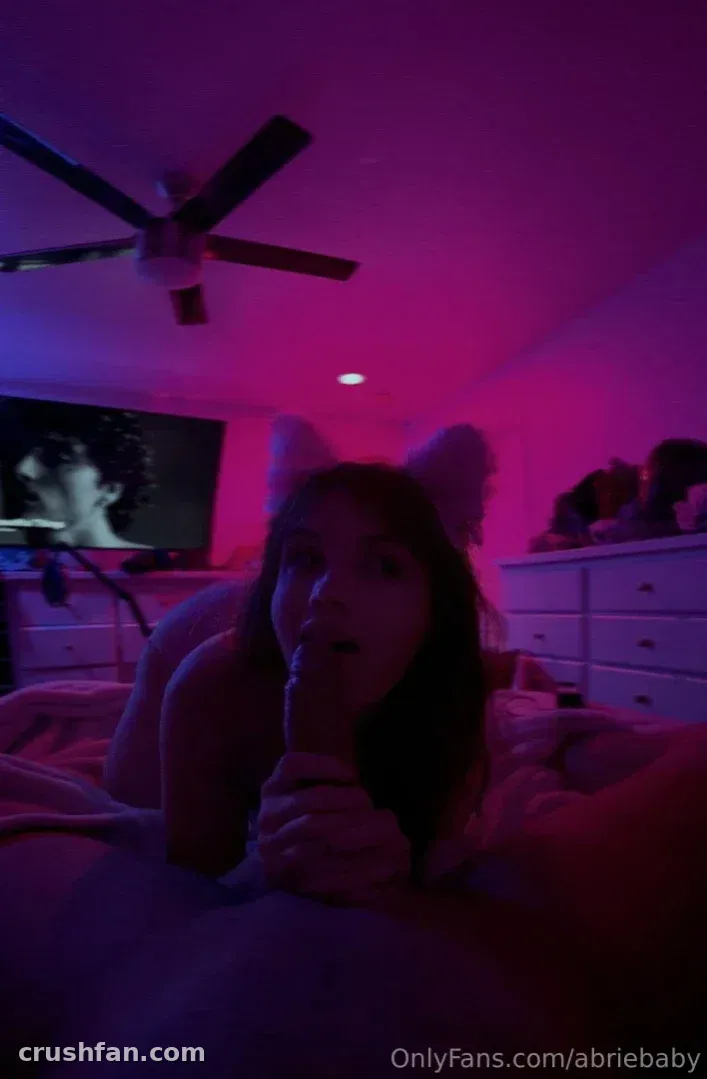 Abriebaby em uma cama em um quarto com luz rosa e um ventilador de teto acima