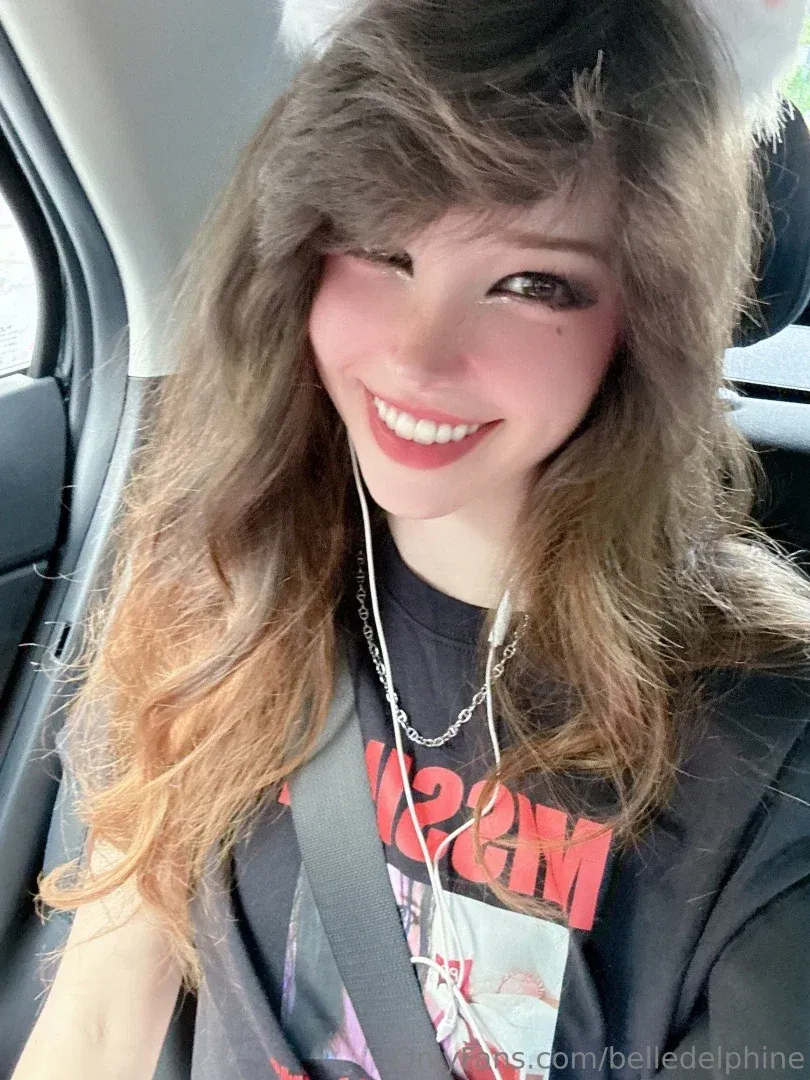 Belle Delphine улыбается на селфи в машине с волнистыми волосами и чёрным топом с принтом.