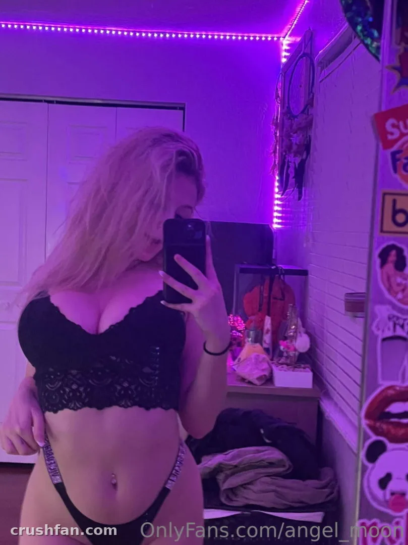 Angel Moon macht ein Spiegel-Selfie in schwarzer Spitzenunterwäsche unter violetter LED-Beleuchtung.