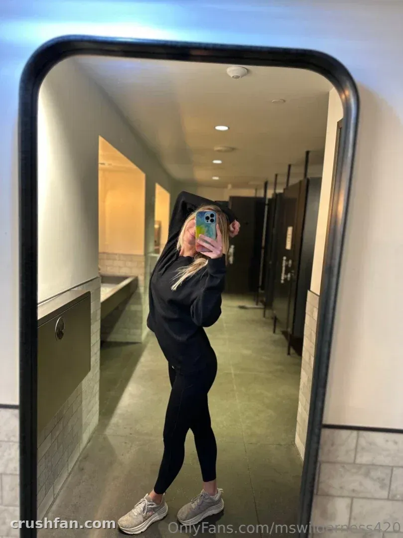 Ms Wilderness in einem schwarzen Hoodie und Leggings beim Spiegel-Selfie in einem Flur