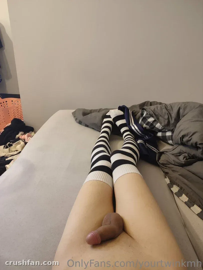 Creator allongé sur un lit portant des chaussettes hautes rayées noir et blanc, une couette grise à côté de lui