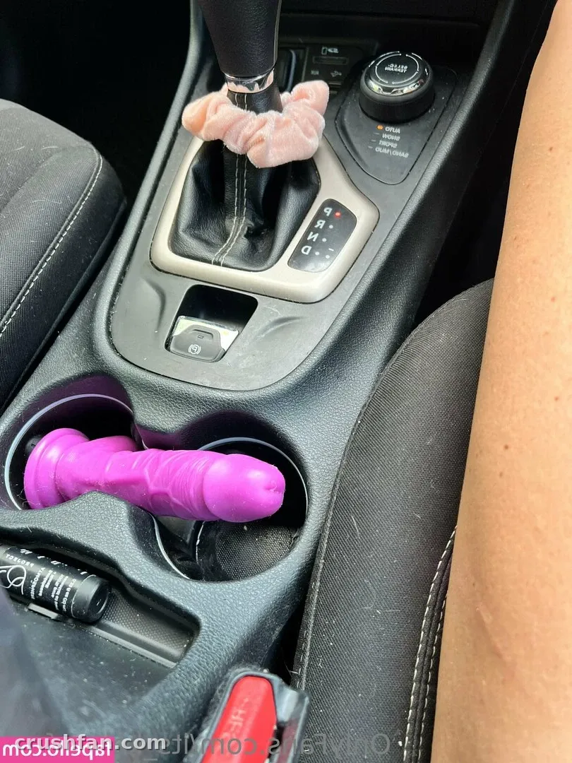 Close view of a car centre console with a pink fabric on the gear stick and a purple item in the cup holder