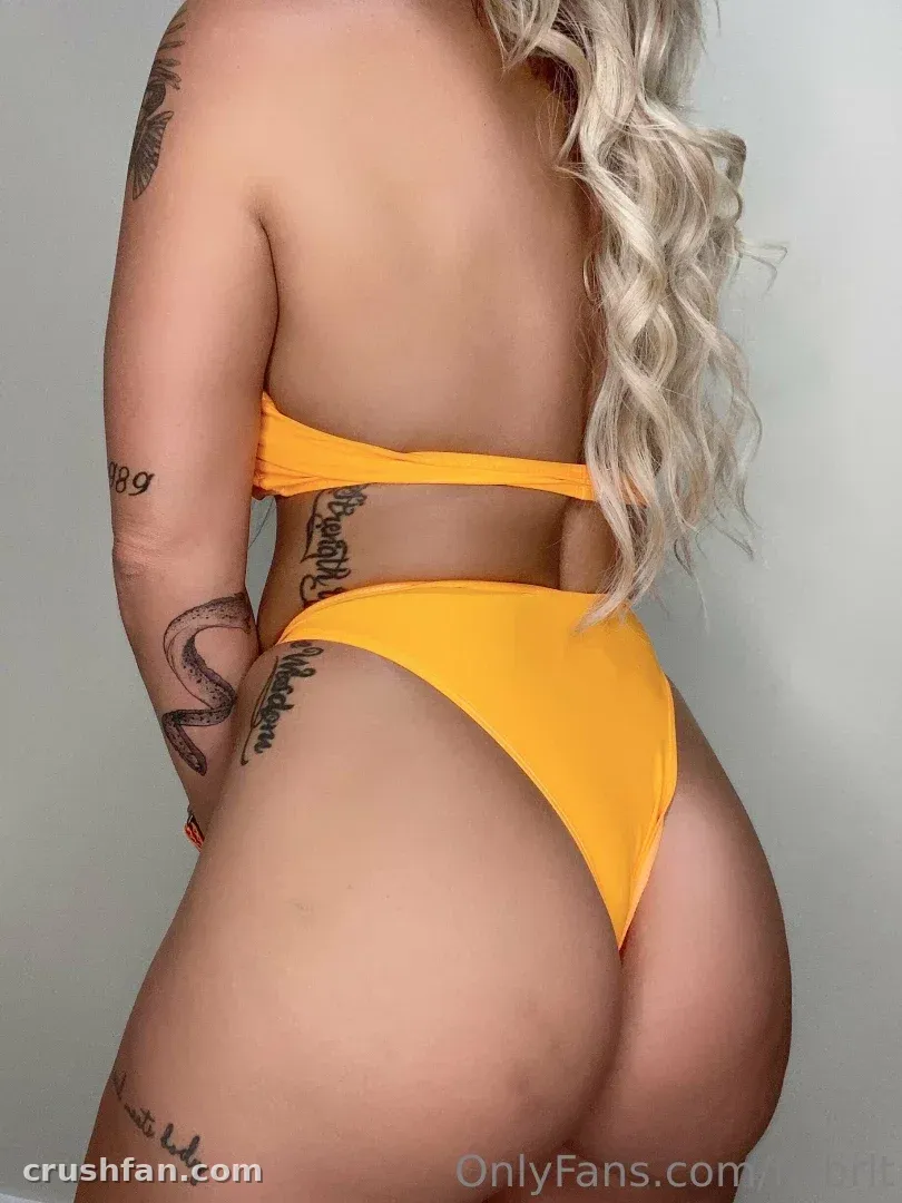 Britt em um conjunto de duas peças amarelo vista de costas contra uma parede lisa