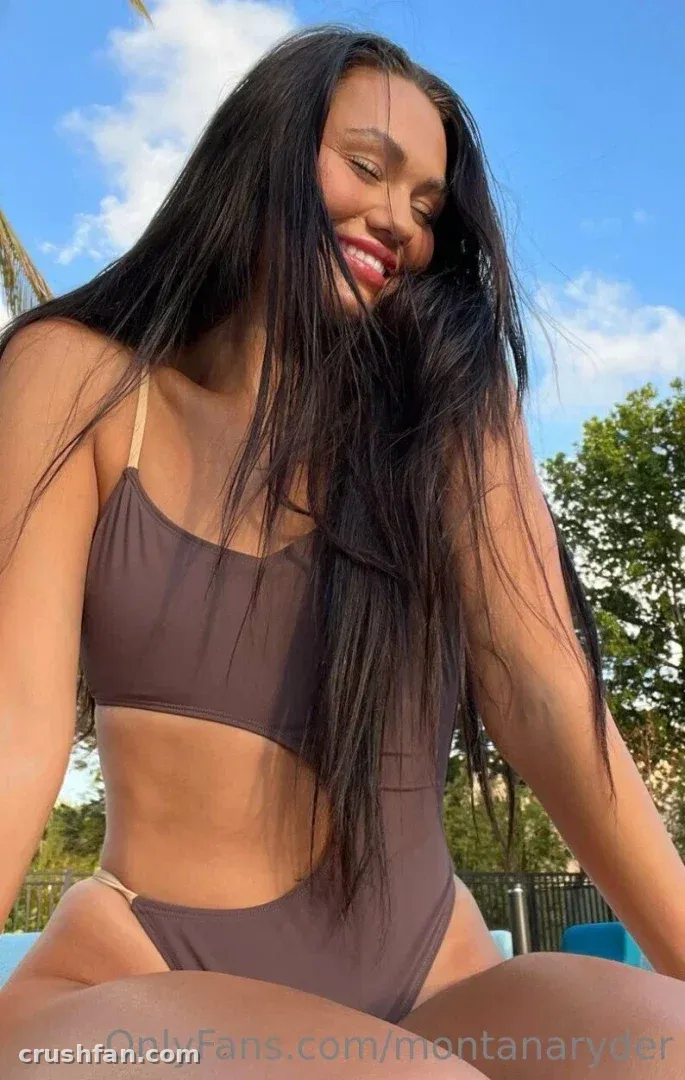 Montana Ryder sonriendo al aire libre con un bikini marrón bajo un cielo azul.