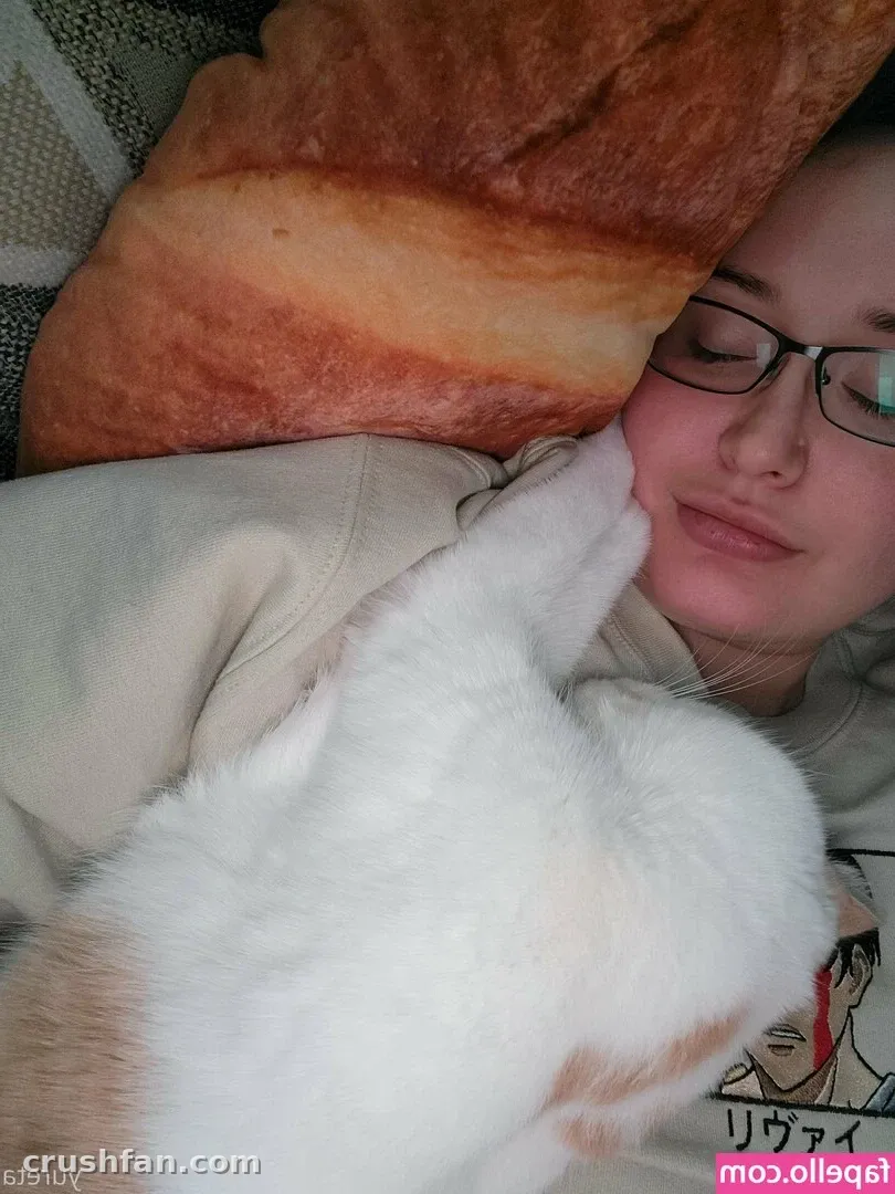 Mulher de óculos descansando ao lado de uma gata branca sobre uma almofada em formato de pão