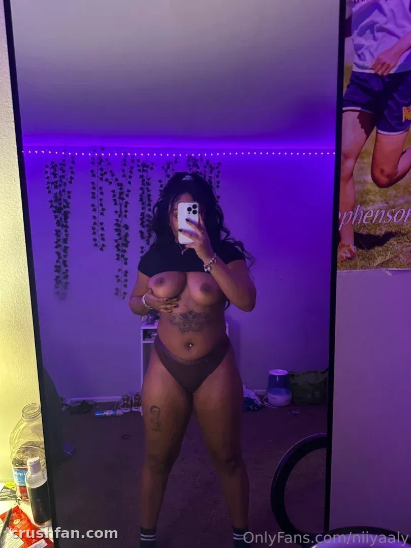 Creator in a dark two-piece outfit taking a mirror selfie in a purple-lit room with hanging plants.