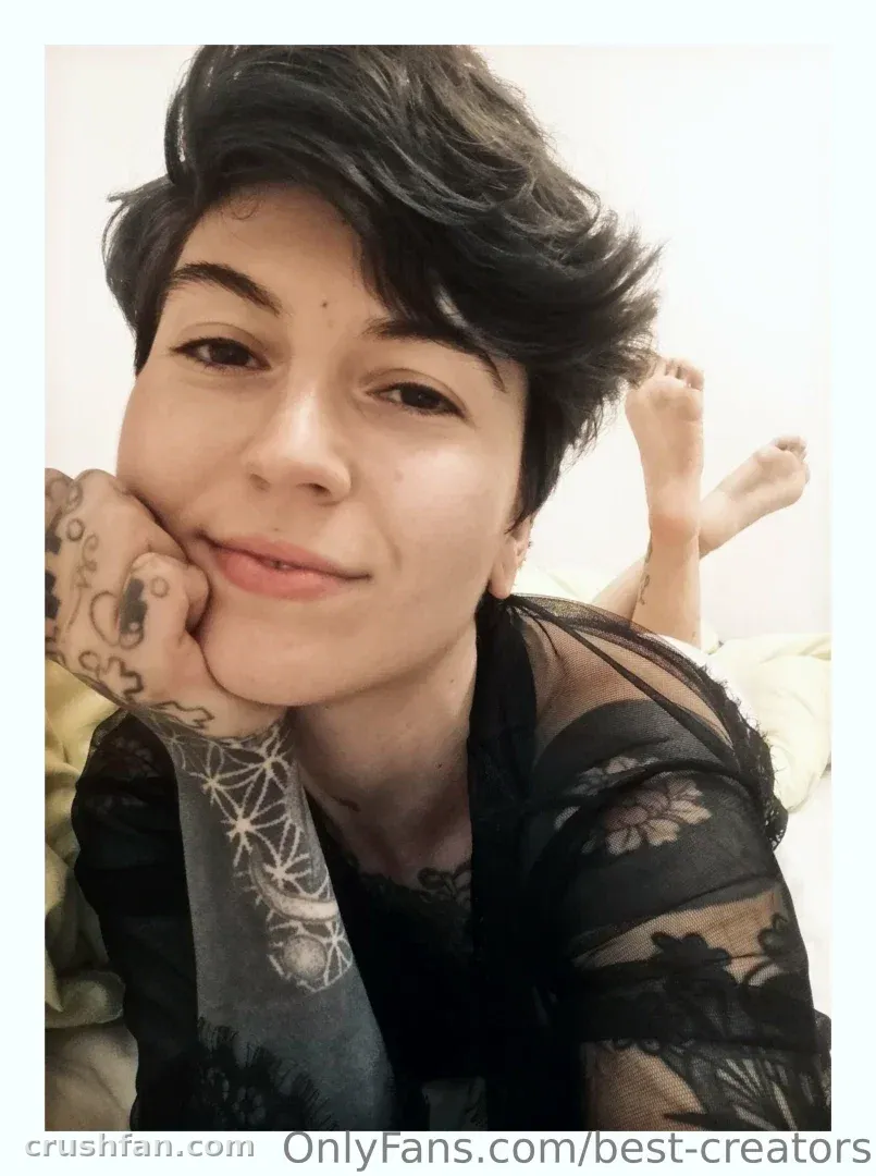 BestCreators em uma peça preta de renda apoiando o queixo na mão em ambiente interno