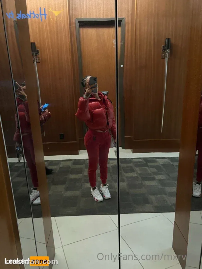 Créatrice en veste doudoune rouge et pantalon prenant un selfie dans le miroir dans une pièce lambrissée de bois