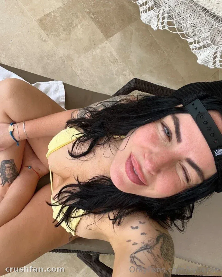 Kylie Rae in a yellow top and black headband winking at the camera outdoors.