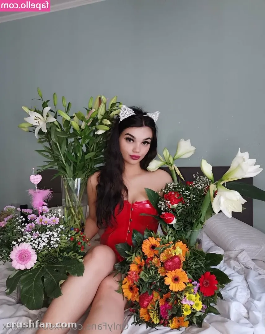 Criadora em um espartilho vermelho sentada em uma cama cercada por lírios brancos e buquês coloridos