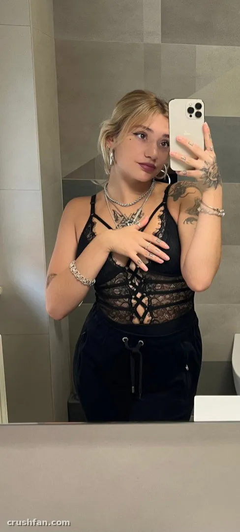 Elizabeth Sanchez in a black lace top taking a mirror selfie in a tiled bathroom.