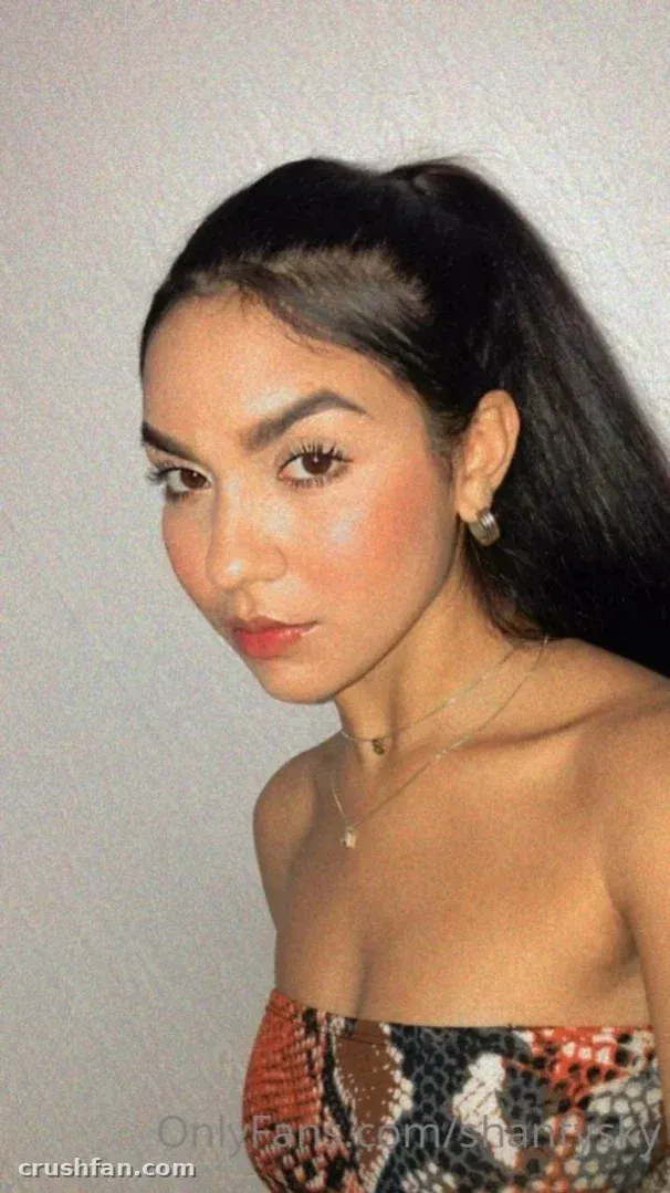 Shantal Sky in a snake-print strapless top and gold necklace against a plain wall