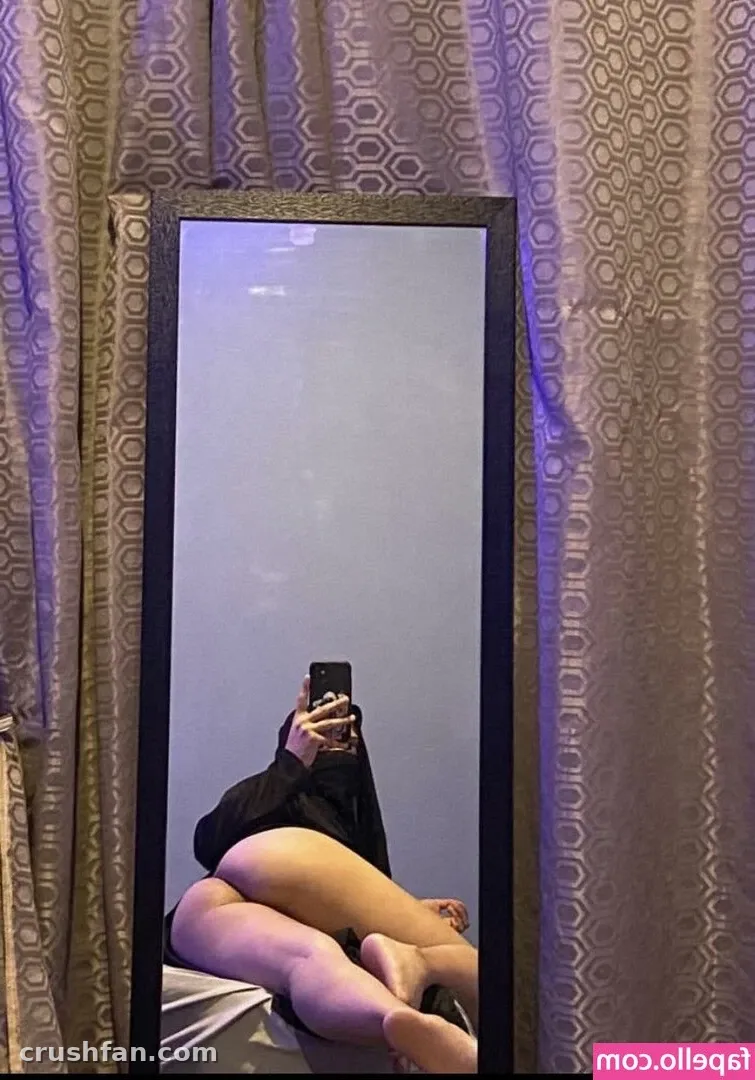 Mirror selfie of a woman seated in front of patterned curtains