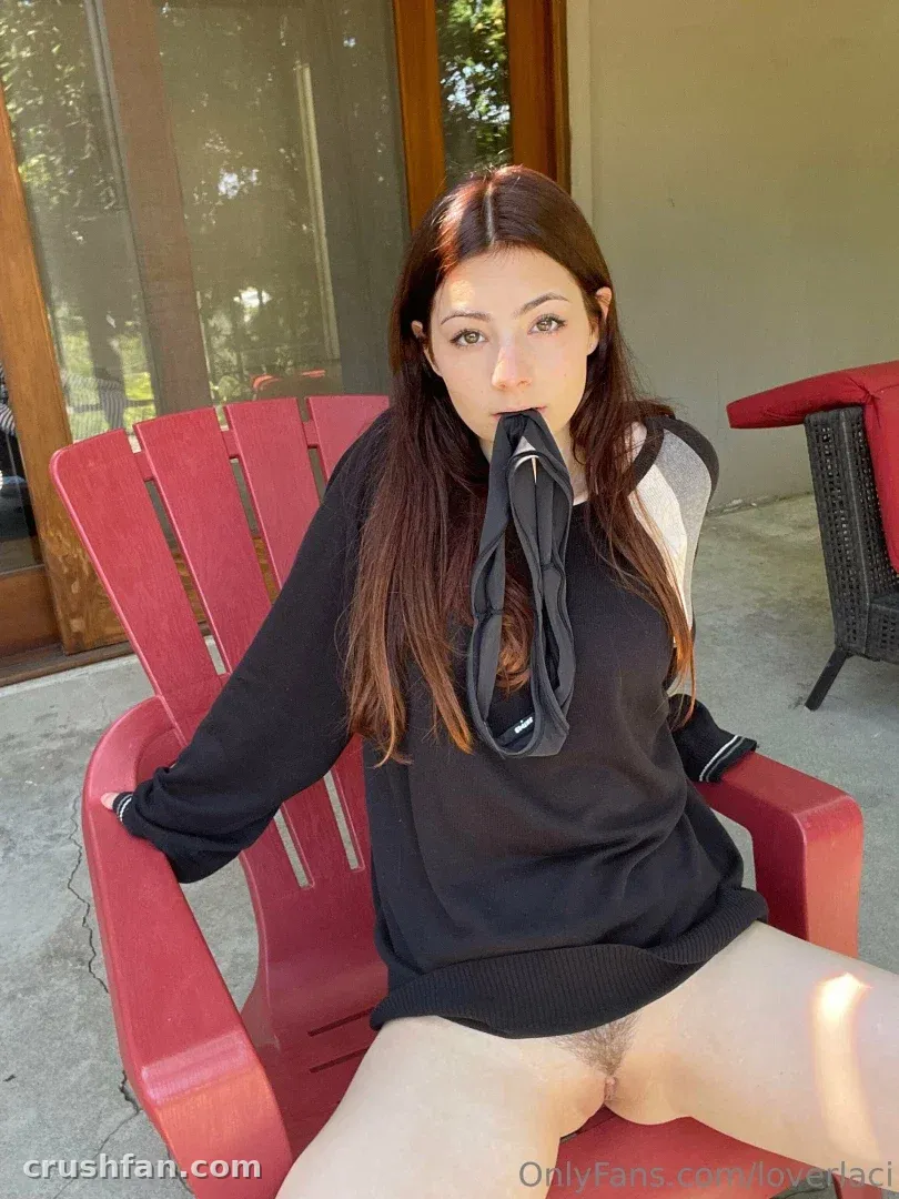 Laci Witton сидит на красном уличном кресле в чёрном топе в залитой солнцем обстановке террасы