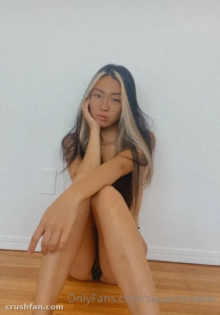 Mila Koi seated on a wooden floor against a white wall in soft light