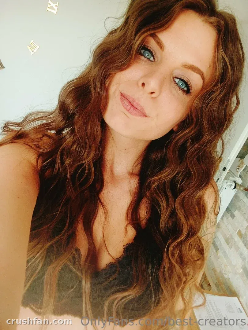 Criadora com cabelo longo, ondulado e castanho tirando uma selfie em ambiente interno com uma blusa escura