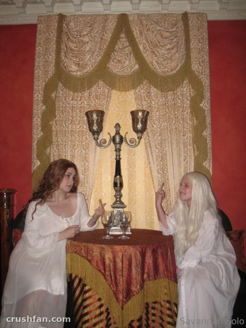 Savannah Solo in a white gown seated at a table with a candelabra against red walls