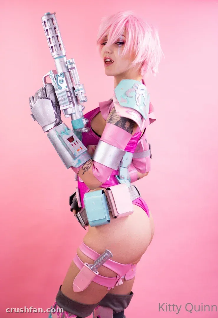 Créatrice avec perruque rose et cosplay futuriste rose et argenté tenant un blaster factice sur fond rose.