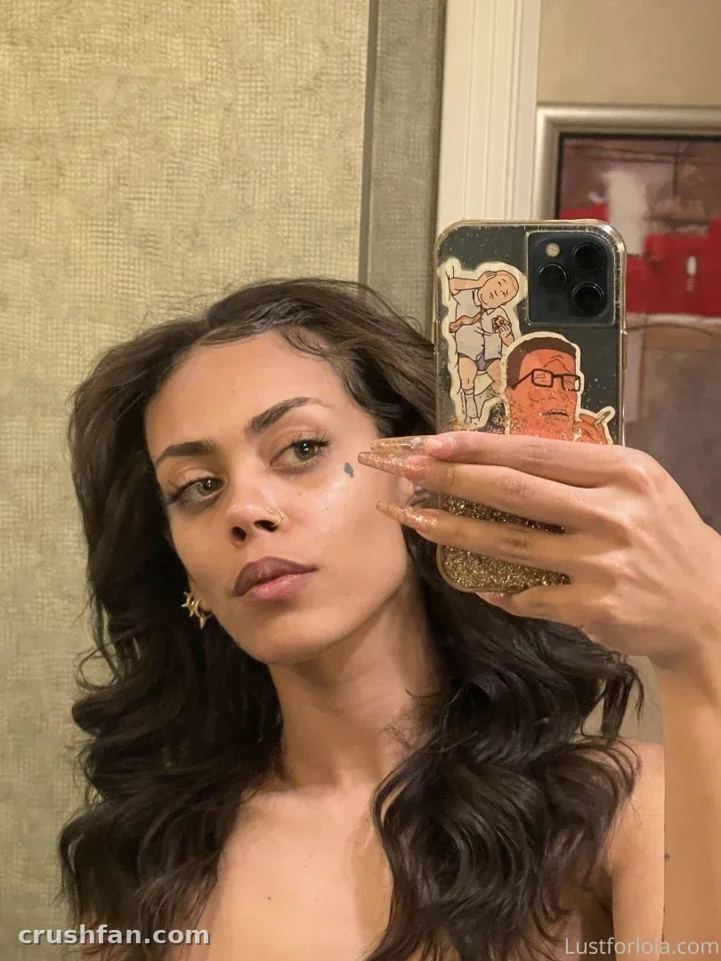 Selfie no espelho de uma mulher com cabelo longo e ondulado segurando um celular coberto de adesivos