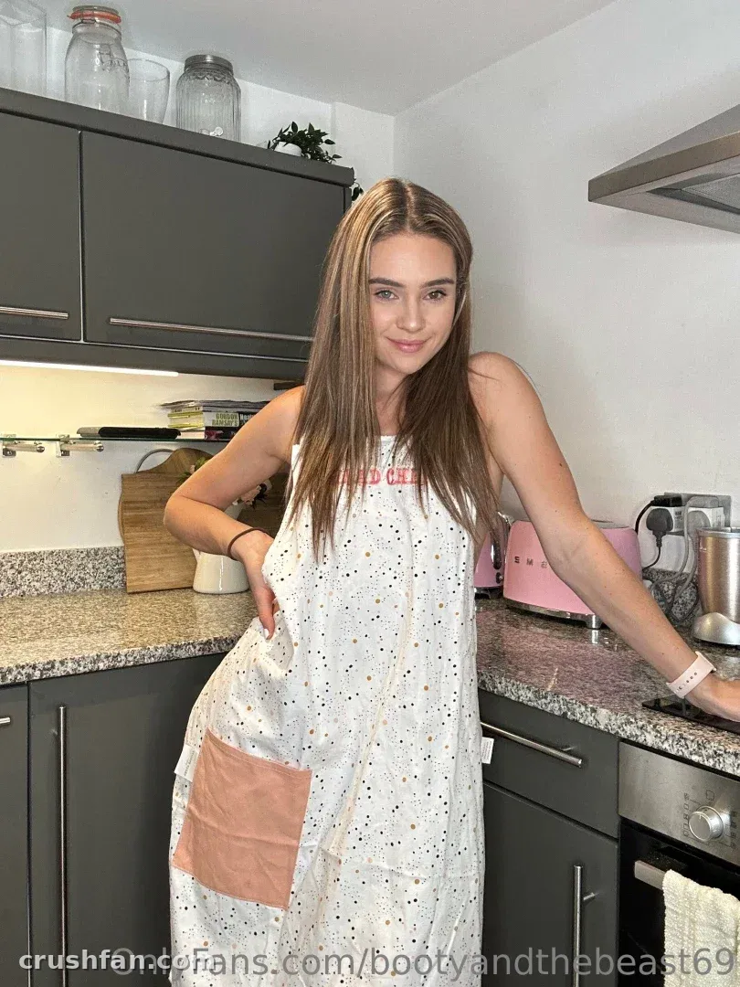 Hannah steht in einer Küche und trägt eine weiße gepunktete Schürze mit einer pfirsichfarbenen Tasche.