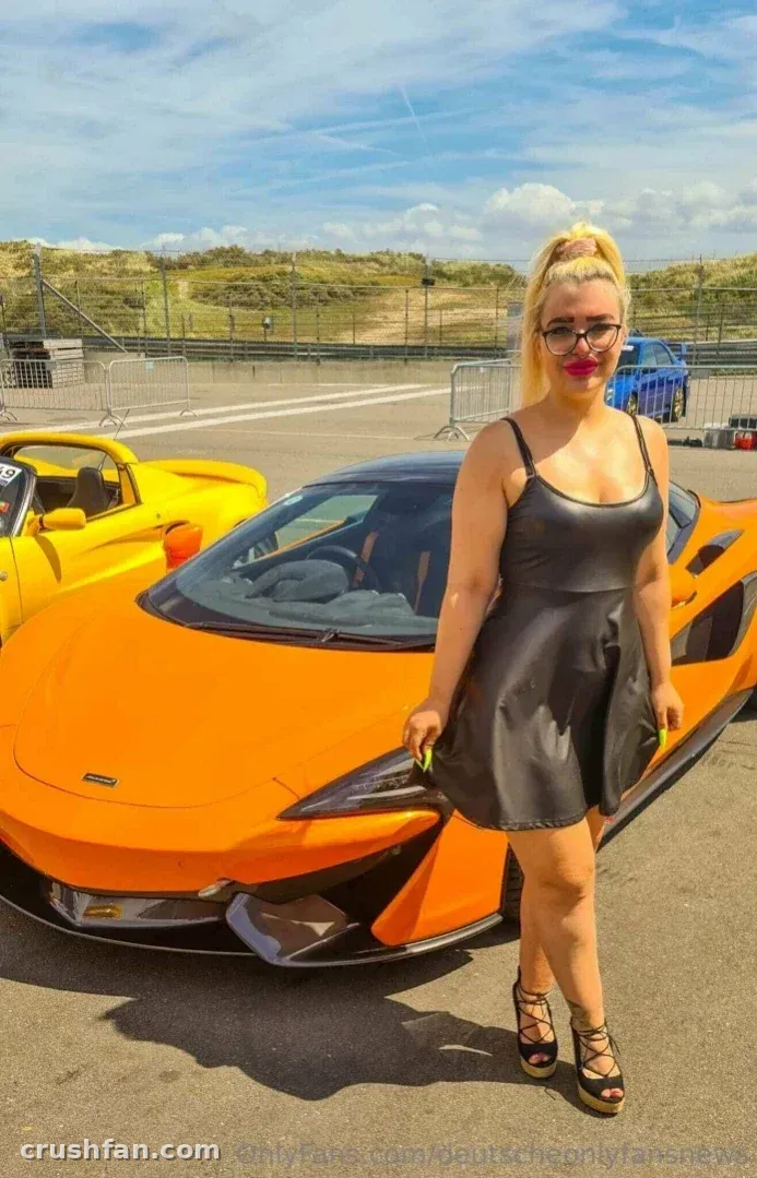 Creator in a black dress standing beside an orange sports car outdoors