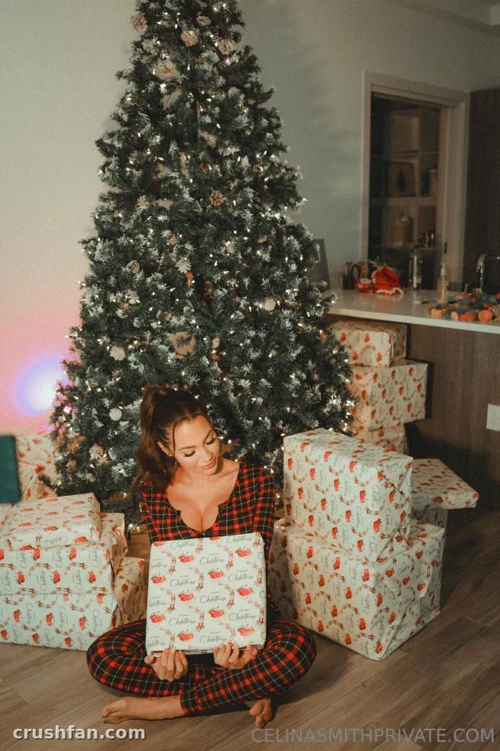 Cel con pijama de cuadros rojos sentada en el suelo junto a un árbol de Navidad iluminado con regalos envueltos