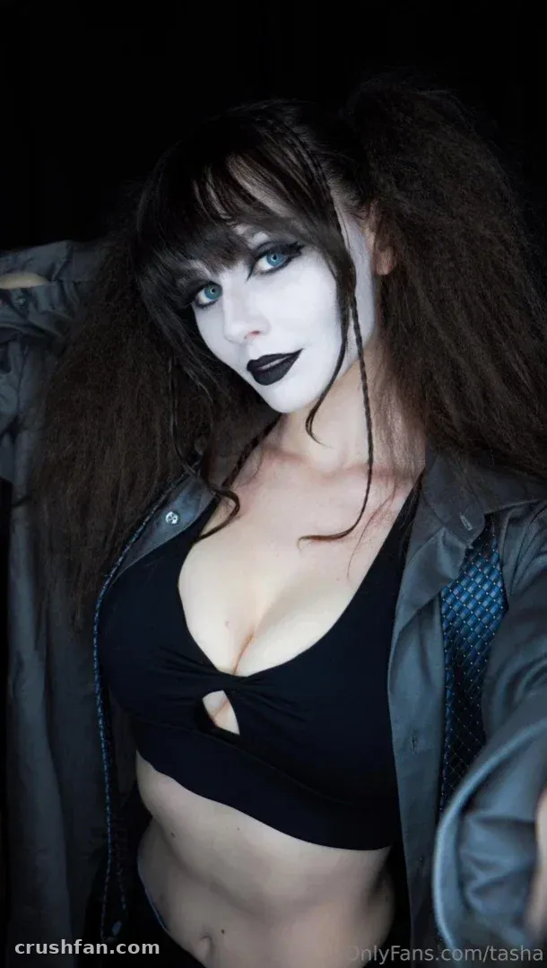 Tasha in a black top and jacket with pale gothic makeup against a dark background