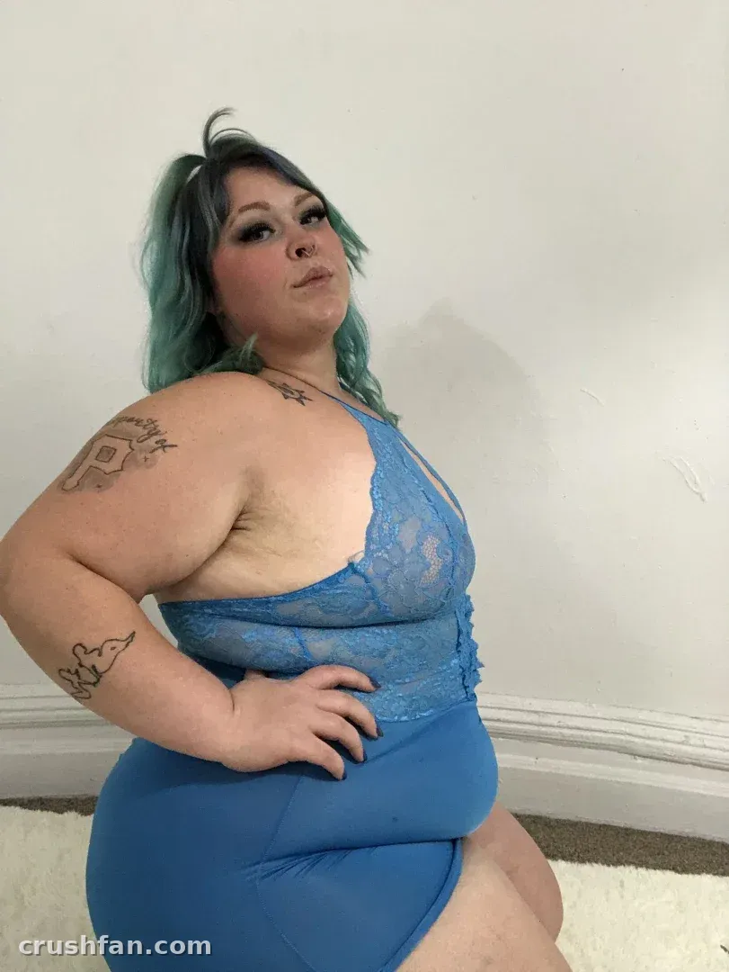 Creator in blue lace lingerie posing indoors against a white wall