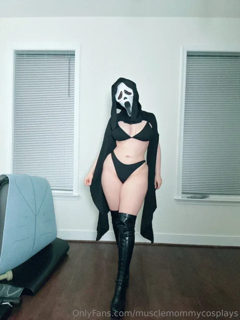 Linnea in a Ghostface mask and black swimsuit with tall boots indoors.