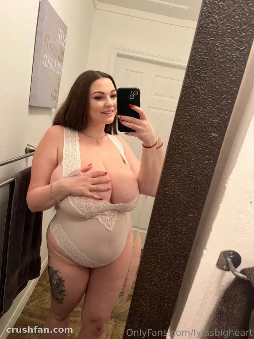 Woman in a cream lace bodysuit taking a mirror selfie in a bright bathroom