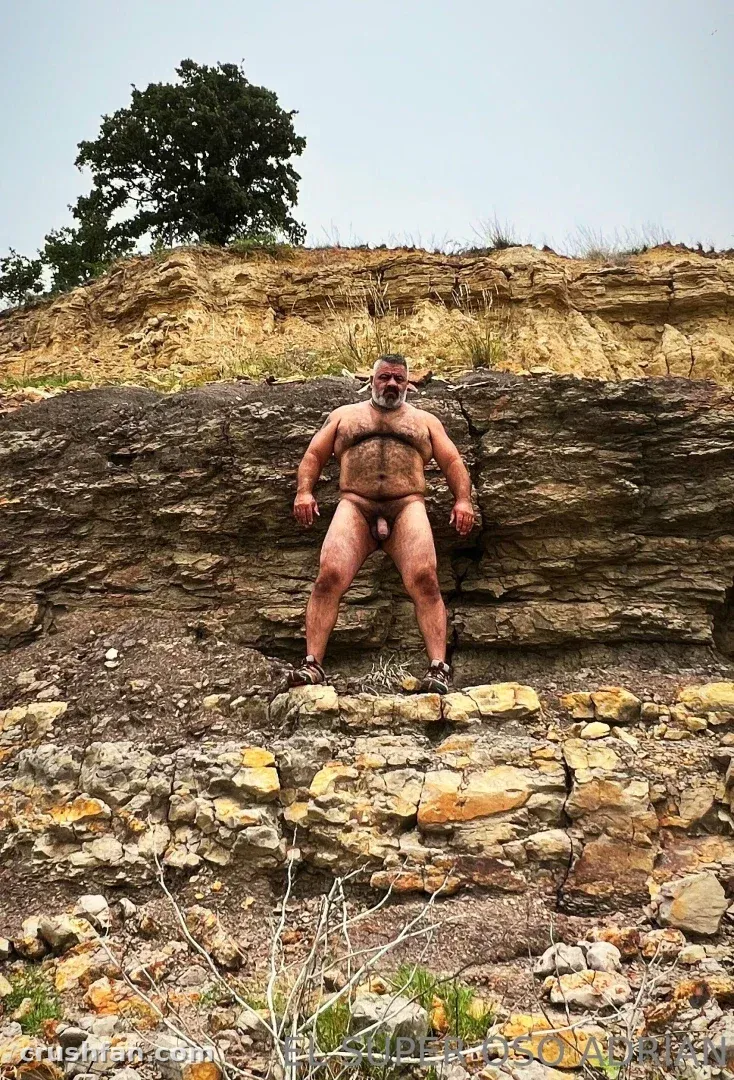Creator standing on a rocky quarry ledge beneath a layered cliff and pale sky