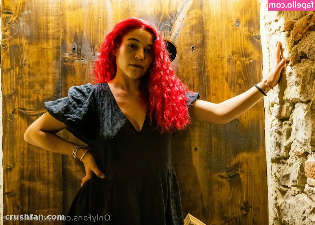 Zlounisko in a black dress leaning by a rustic wooden door with a stone wall beside her